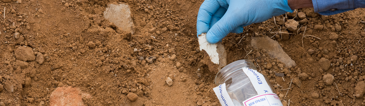 Gloved hand placing asbestos in specimen jar