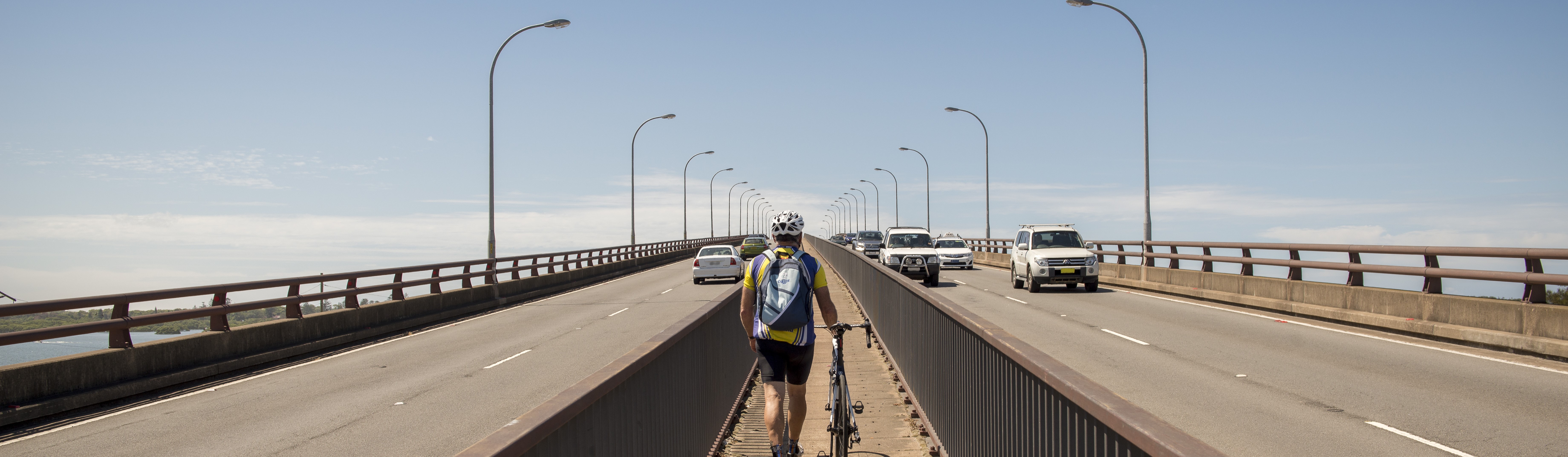 Cyclist walks over bridge with bike, cars on road