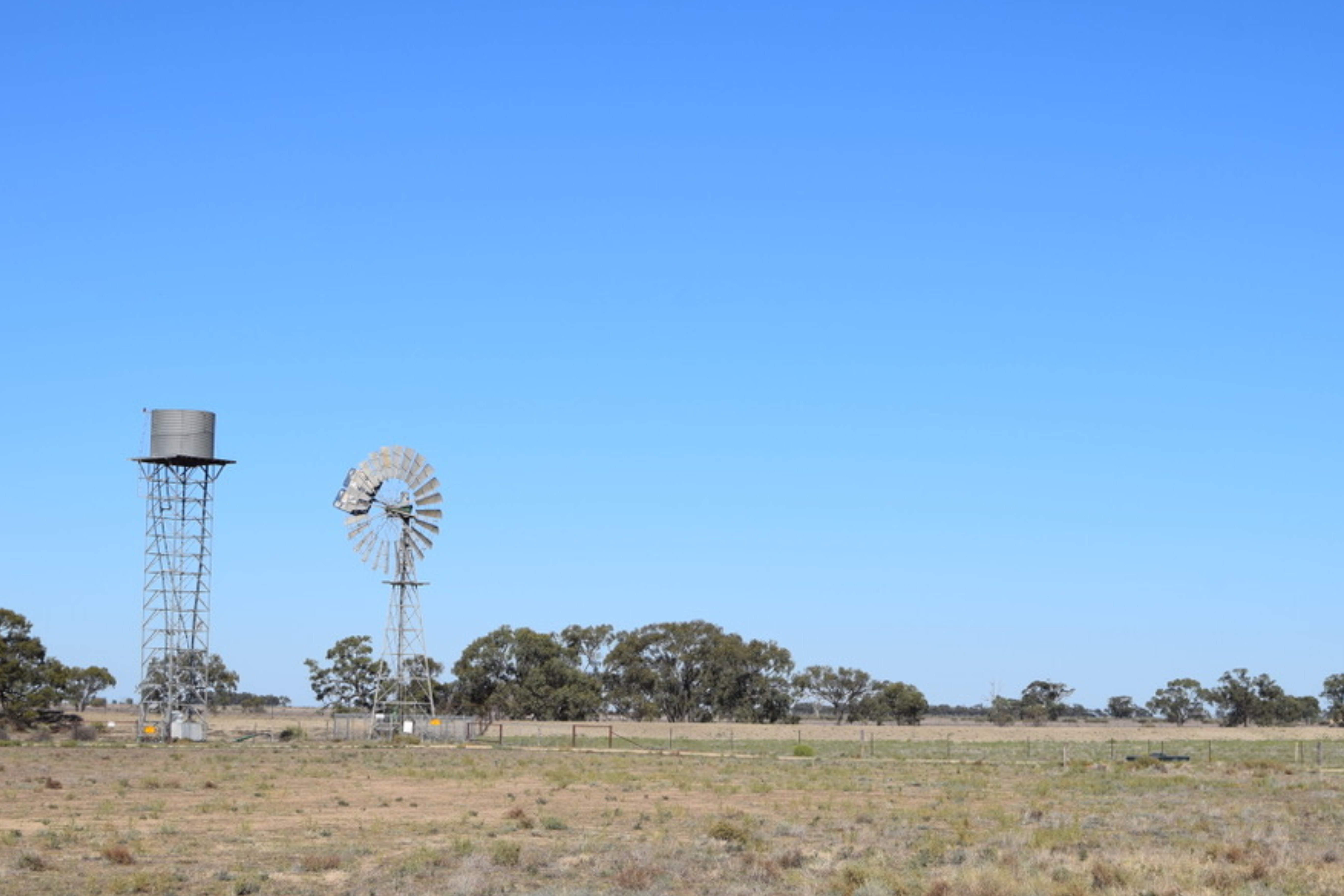 View across dry paddock in Hay with water towers on skyline