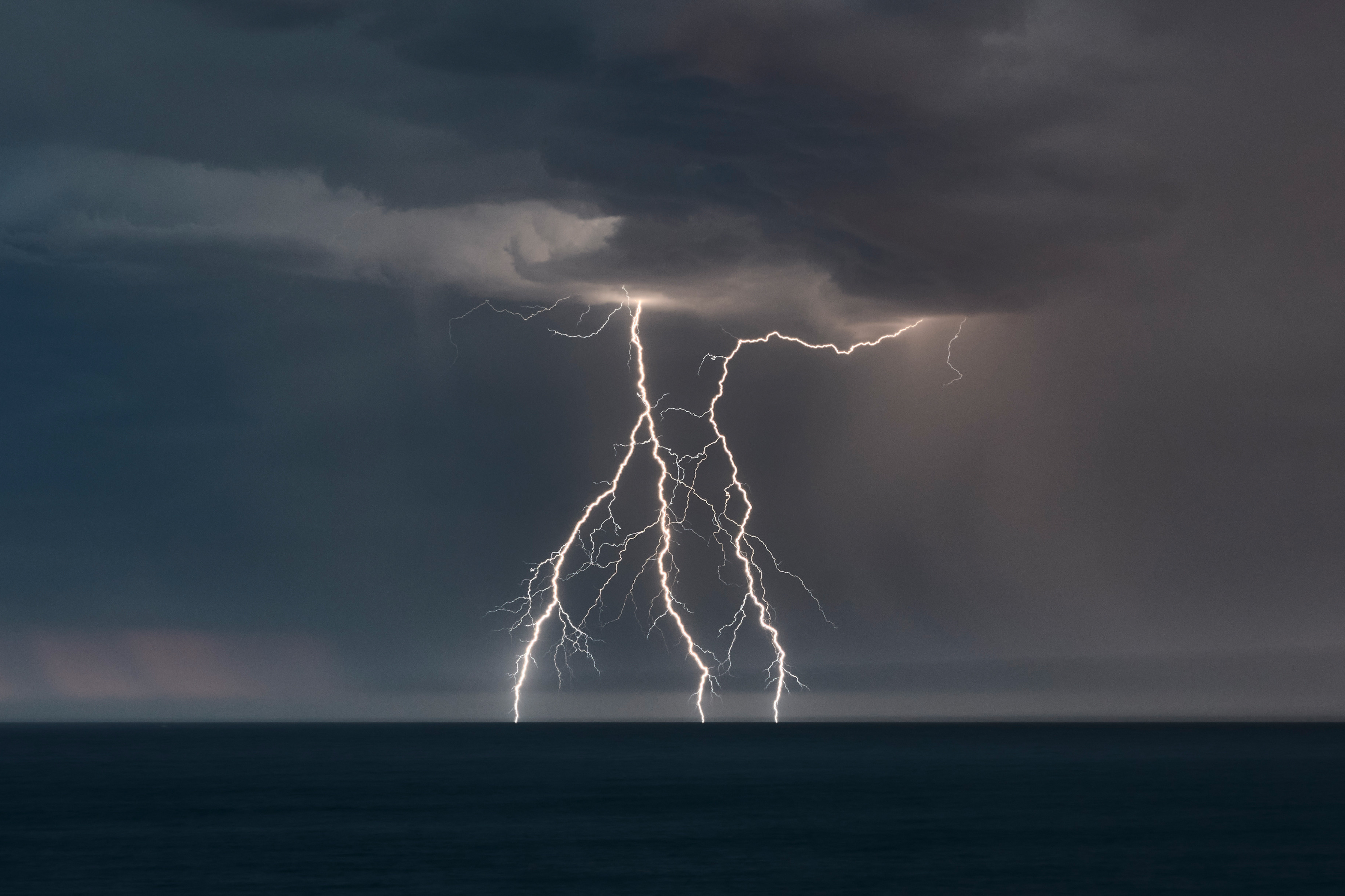 Multiple lightning strikes across open water, evening storm