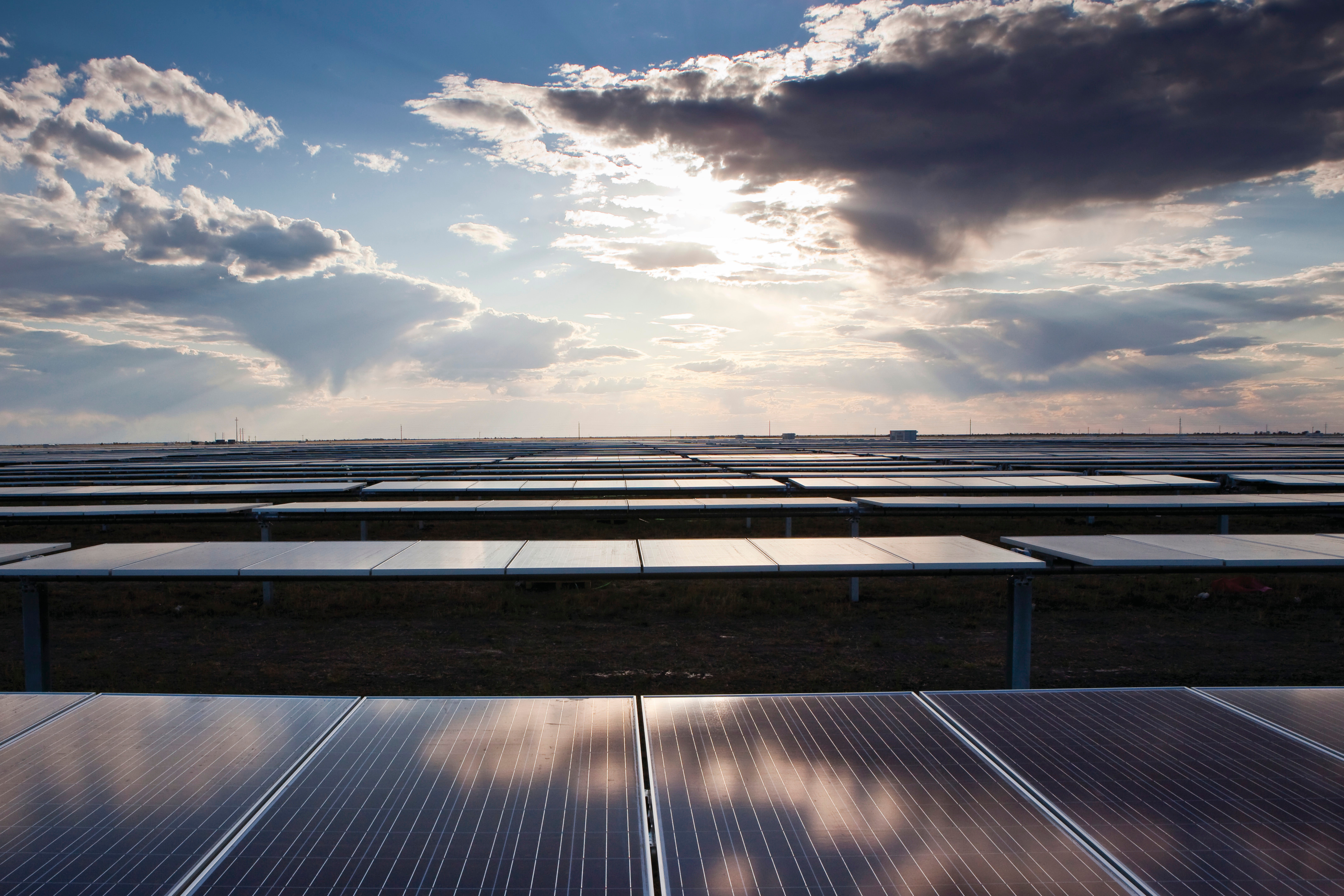 Looking across a solar farm, with reflections of sunlight through stormy clouds visible on solar panels