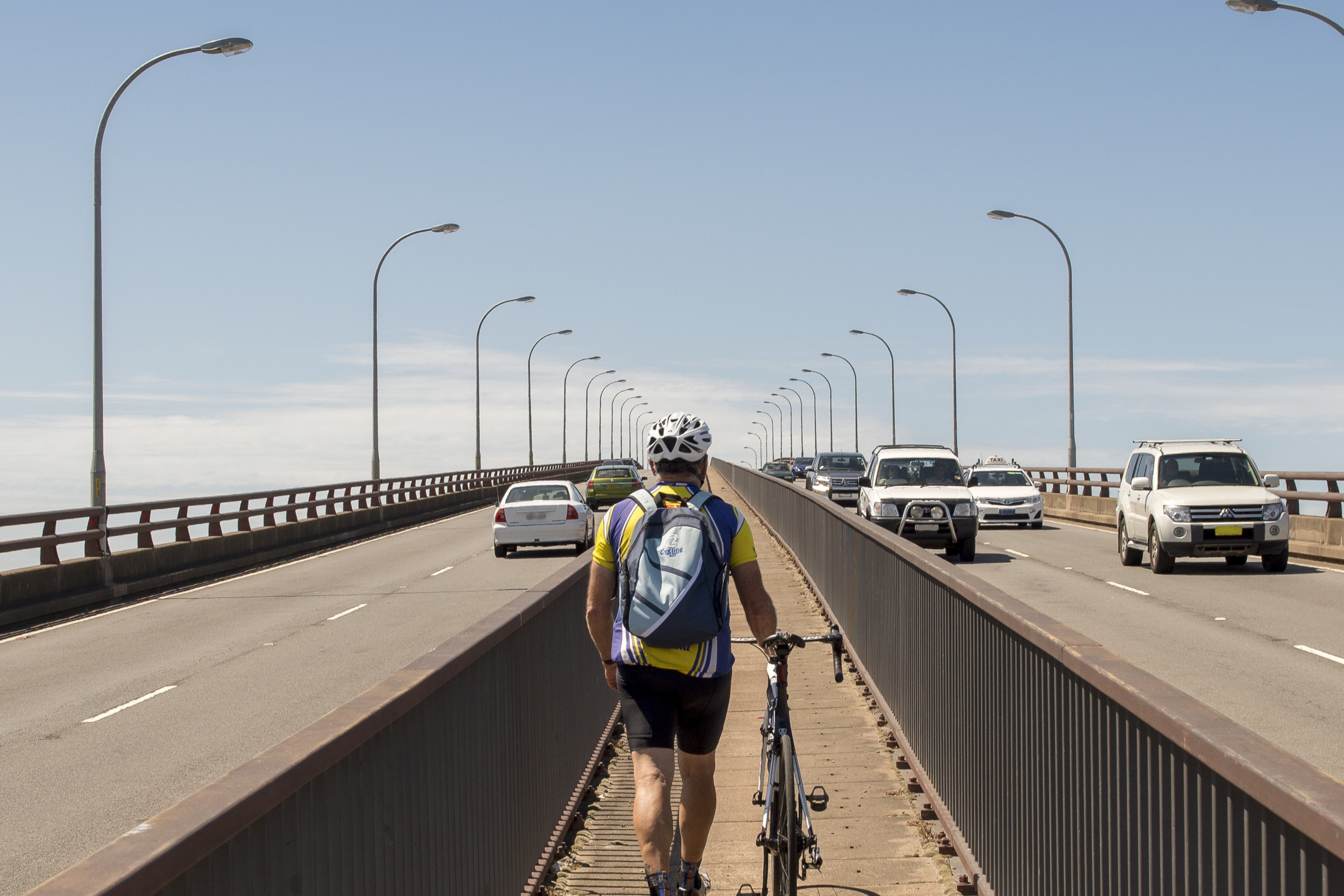 Cyclist walks over bridge with bike, cars on road